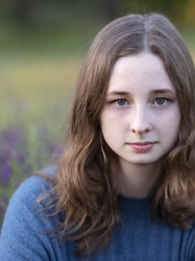 Blue eyed girl sitting in a field of purple flowers.