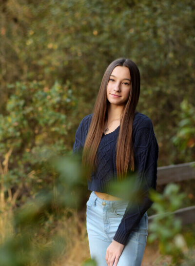 Long haired brunette girl standing near a brown wood fence.