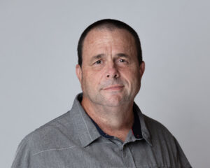 Headshot of a man wearing a grey shirt on a light grey backdrop.