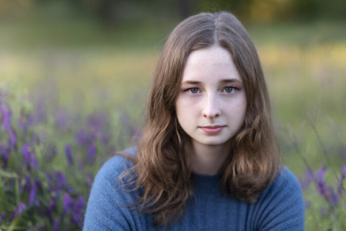 Blue eyed girl sitting in a field of purple flowers.